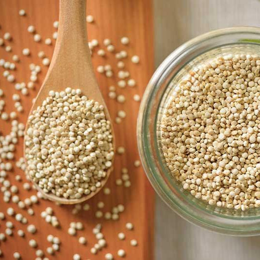 Glass jar and wooden spoon filled with quinoa, light-colored seeds on a wooden surface.