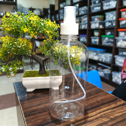Clear spray bottle with white nozzle on a wooden surface, with a blurred indoor setting in the background.