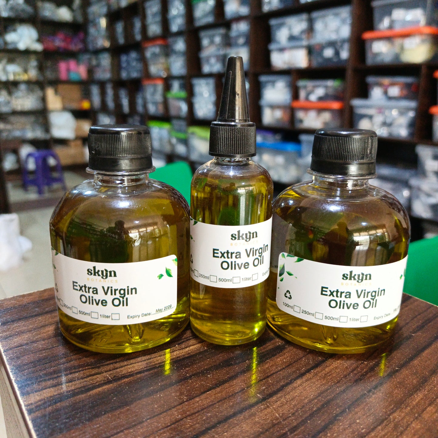 Three bottles of skgn Extra Virgin Olive Oil on a wooden surface with a store shelf in the background.