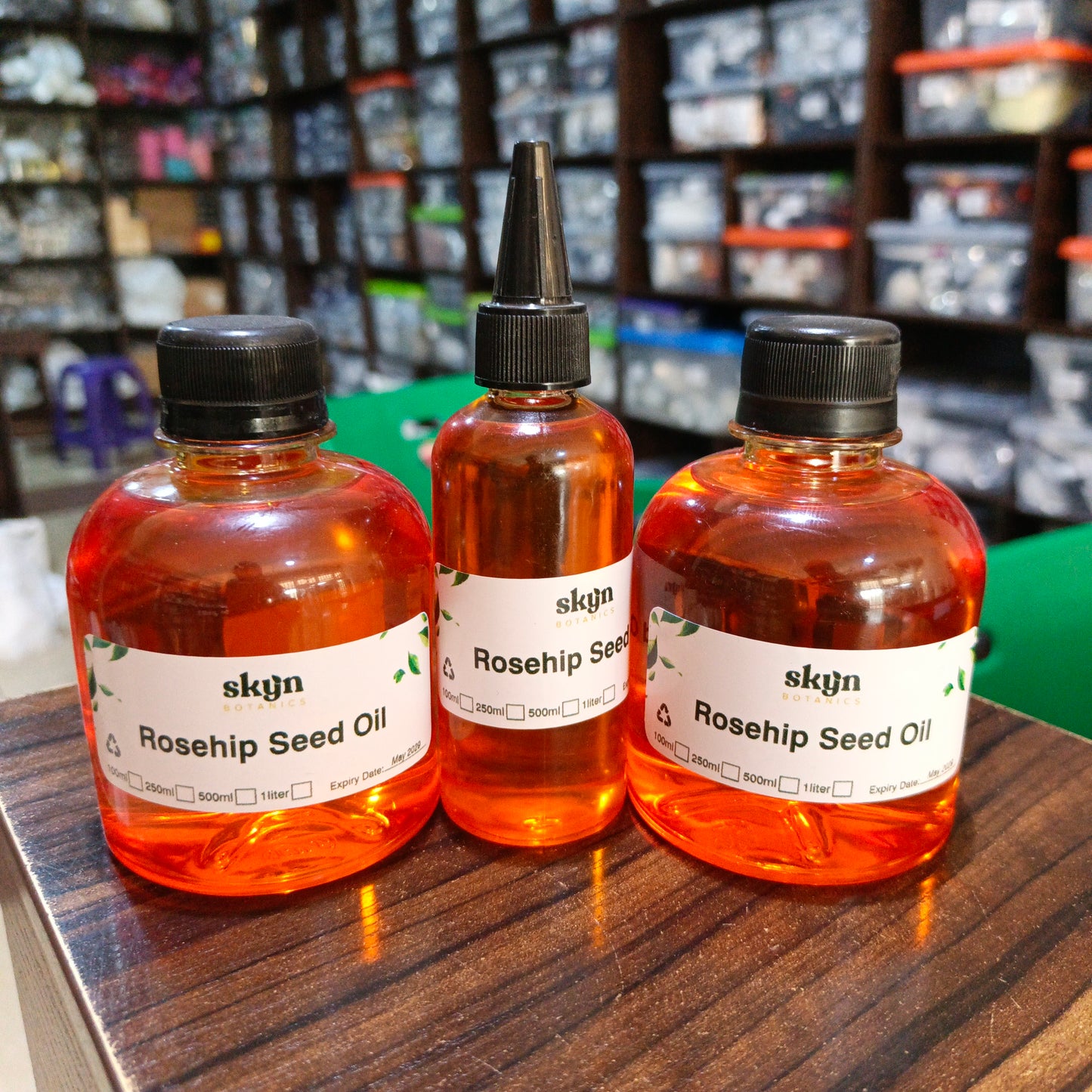 Three bottles of skyn Rosehip Seed Oil on a wooden surface with shelves in the background.