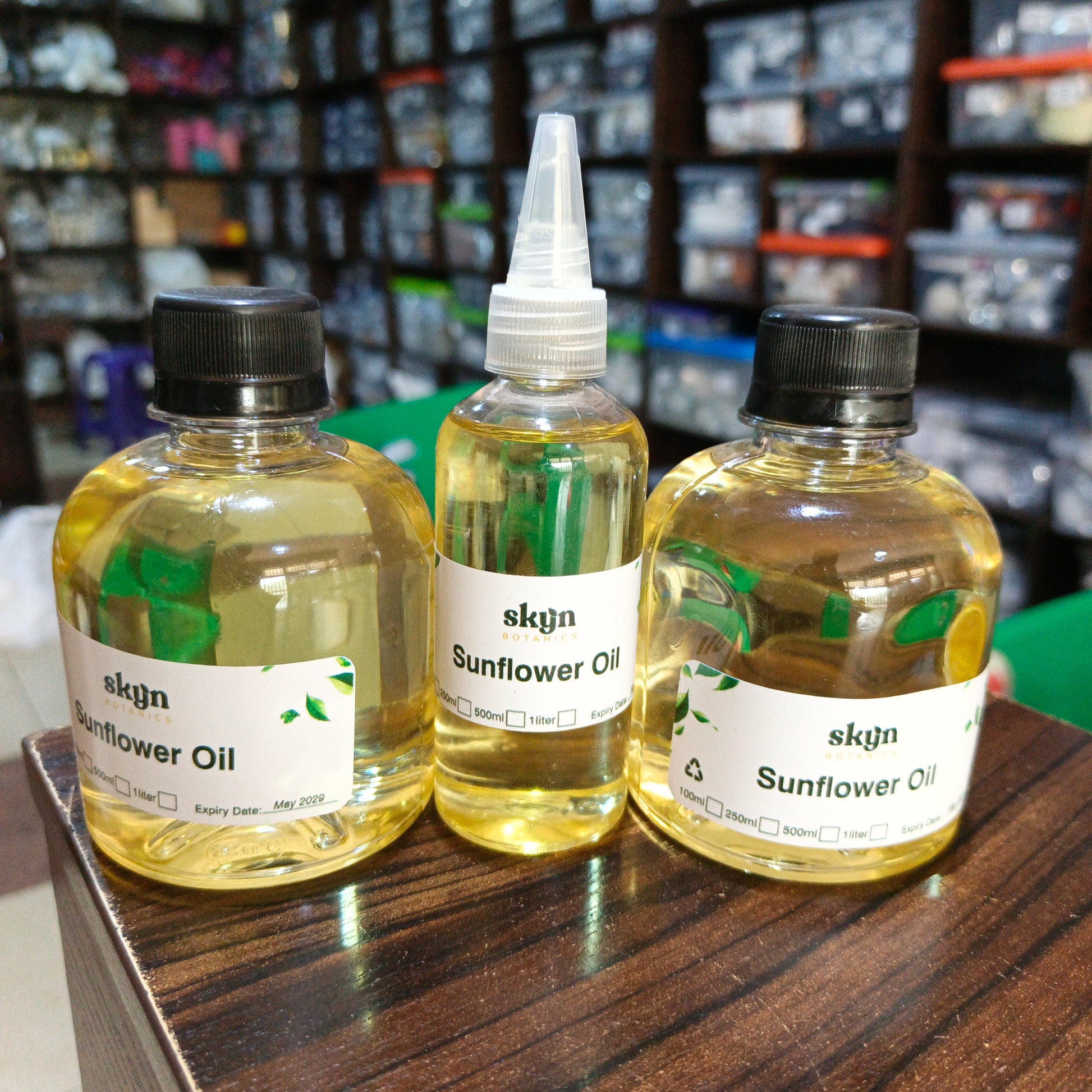 Three bottles of sunflower oil with labels on a wooden surface, with shelves in the background.